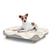 Hund sitter på en liten Topology hundbädd med fårskinnsöverdrag och runda träfötter