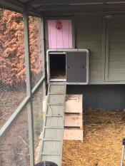 En Autodoor som är kopplad till en stor hönsgård i trä med en ramp upp till dörren.