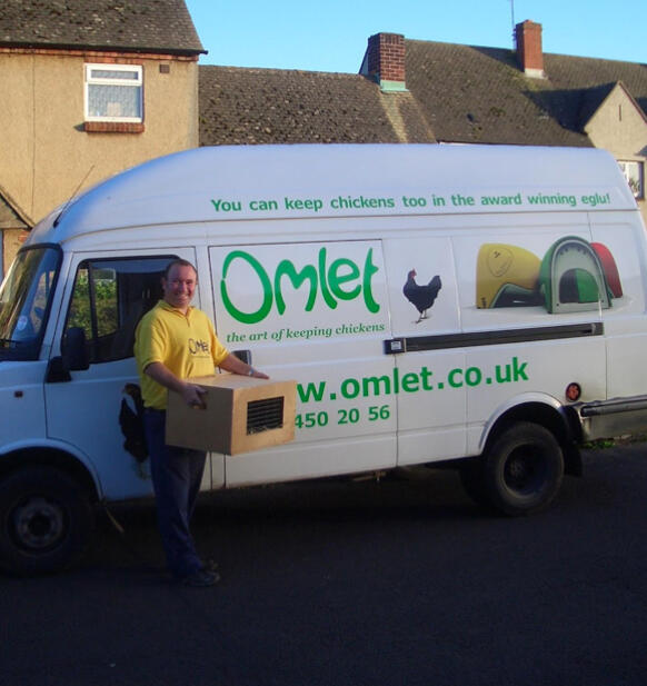 En leveransförare bredvid en skåpbil med varumärket Omlet med en låda med kycklingar