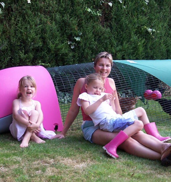 En familj sitter bredvid en rosa Eglu hönsgård
