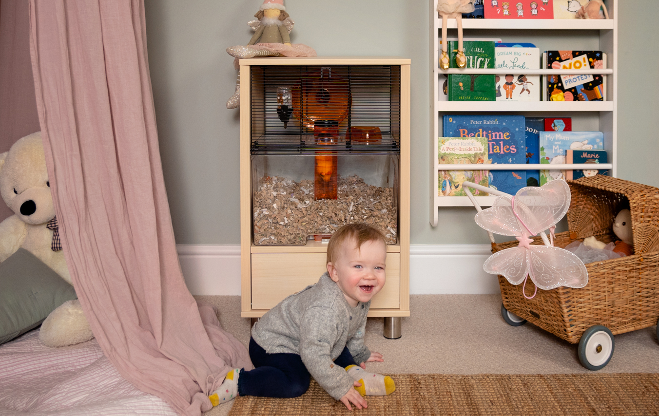 ett litet barn leker i sitt sovrum och det står en hamsterbur i bakgrunden
